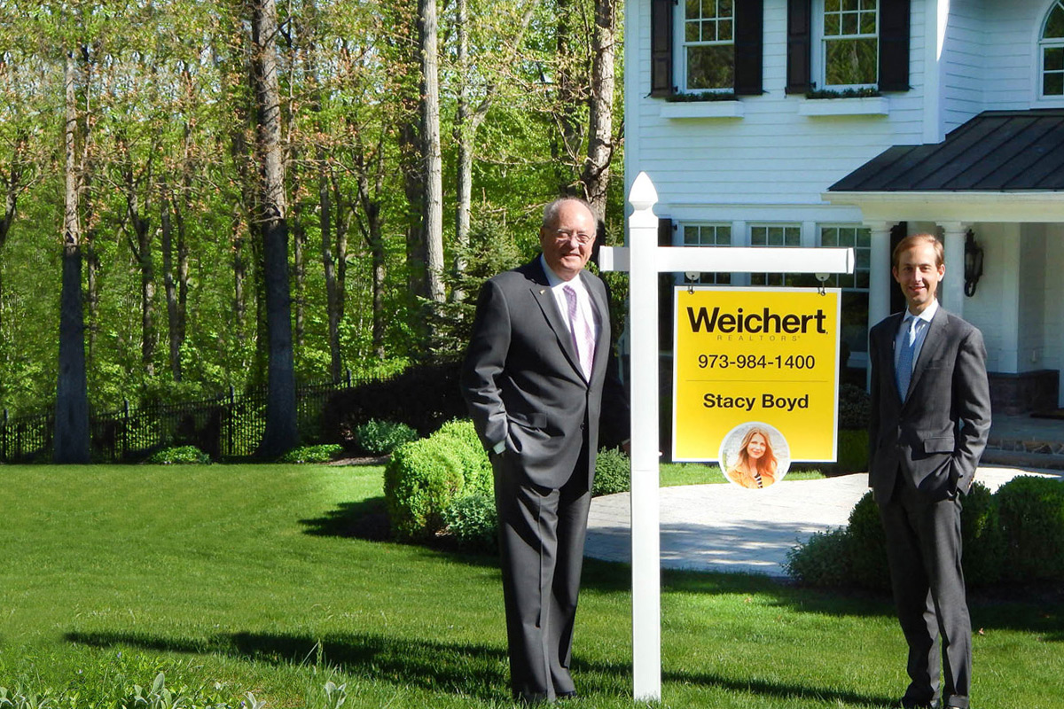 Jim Weichert and James Weichert standing by a Weichert property sign